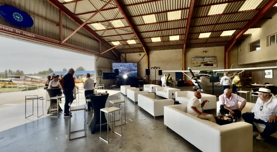 Le hangar de l'Aéro-Club Paris-Nord aménagé en salon pour le Fly-in : canapés, mange-debout et écran, porte ouverte sur la piste